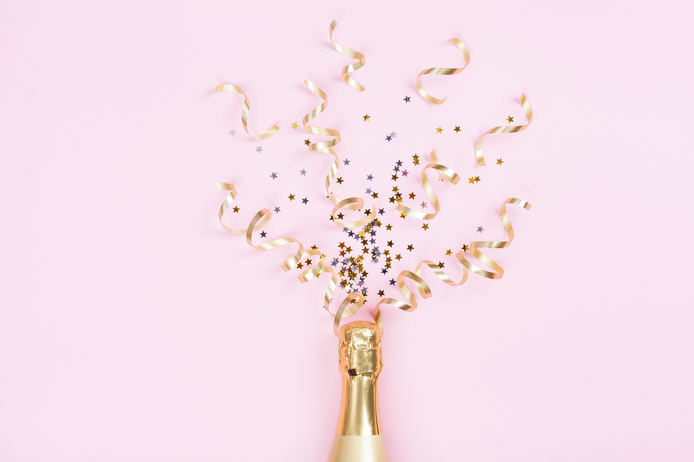 Champagne bottle with confetti stars and party streamers on pink background. Christmas, birthday or wedding concept. Flat lay.